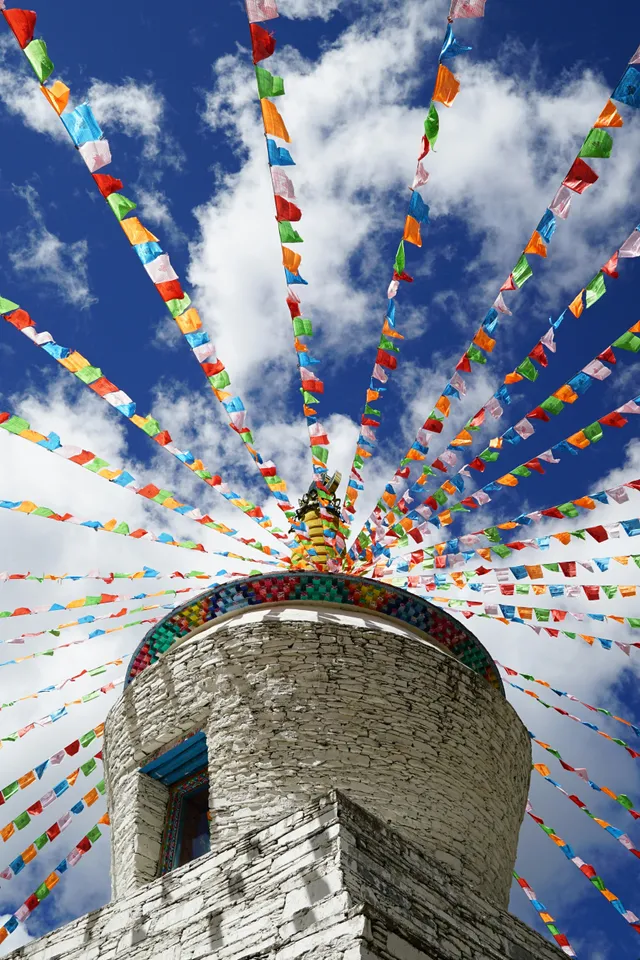 A white Tibetan stupa with colourful prayer flags radiating out against a deep blue sky